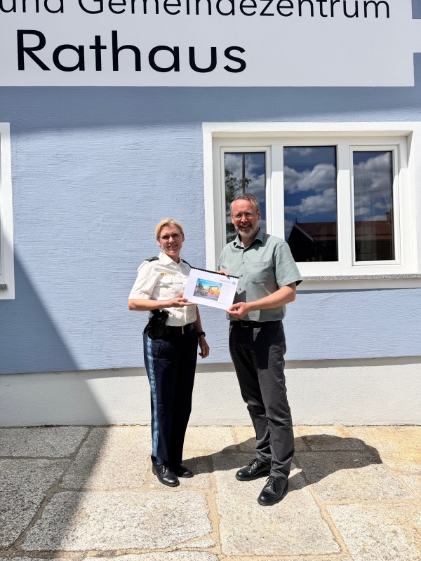 PORin Ingrid Grötzinger übergibt Bgm. Jürgen Schano den Sicherheitsbericht Eine Polizistin und ein Mann stehen vor dem Rathaus in Grainet und halten gemeinsam ein Dokument in die Kamera.