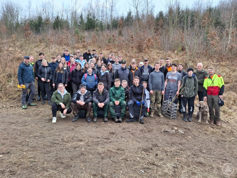Die Schülerinnen und Schüler der R9 und M10 mit den Klassenlehrern und Forstexperten. Die Schüler pflanzten insgesamt 1.200 Setzlinge im Rahmen des Aufforstungsprojektes. Eine große Gruppe von Schülern und Erwachsenen steht auf einer Waldlichtung. Viele tragen Outdoor-Kleidung, einige haben Werkzeuge oder Setzlinge in der Hand. Die Gruppe sieht zufrieden aus, vermutlich nach einem erfolgreichen Pflanzprojekt.