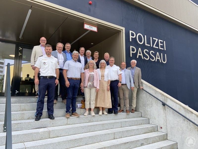 von links nach rechts, obere Reihe: Rudolf Müller, Wolfgang Lindmeier, Stephan Dorn, Josef Artmann, Franz Eibl, Karin Sedlmeier, Walter Knoller, untere Reihe: POR Sebastian Feucht, Erwin Braumandl, Christine Weinberger-Loos, Andrea Koller, PD Christian Dichtl, Christian Fürst, Manfred Hammer Eine Gruppe von rund 15 Personen, darunter mehrere Bürgermeister und Polizeibeamte, steht auf der Treppe vor dem Eingang zur Polizeiinspektion Passau. Alle Personen blicken freundlich in die Kamera. Rechts ist groß der Schriftzug „Polizei Passau“ an der Gebäudefassade zu lesen.