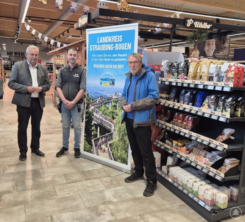 Drei Männer stehen in einem Supermarkt neben einem Regal mit Lebensmitteln. Hinter ihnen ist ein Banner mit der Aufschrift „Landkreis Straubing-Bogen – Machen auch Sie mit!“ aufgestellt.