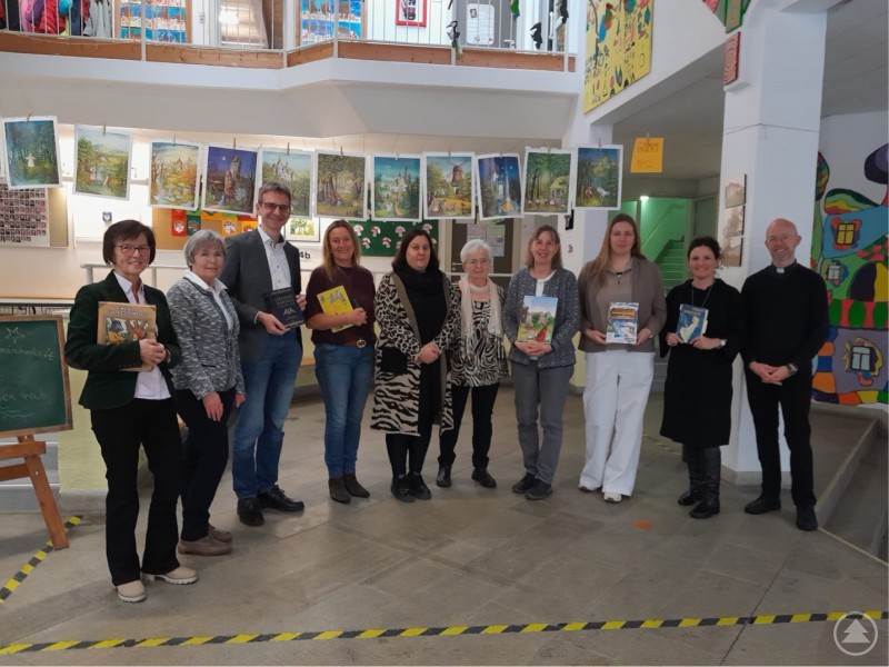 v. l. Frau Kalenda, Frau Reitmaier-Ranzinger, 1. Bürgermeister Roth, 3. Bürgermeisterin Proßer-Greß, Frau Wosnitza, Frau Seidl, Fr. Pöhn, Frau Kashuba, Rektorin Lerach und Pfarrer Keilhofer mit Märchenbüchern Eine Gruppe von zehn Personen steht in einer Grundschule vor bunten Kinderzeichnungen und hält Märchenbücher in den Händen. Im Hintergrund sind zahlreiche gemalte Märchenbilder aufgehängt. Die freundliche Runde besteht aus Vorlesern und Schulvertretern, die an einer Vorleseaktion teilnehmen.