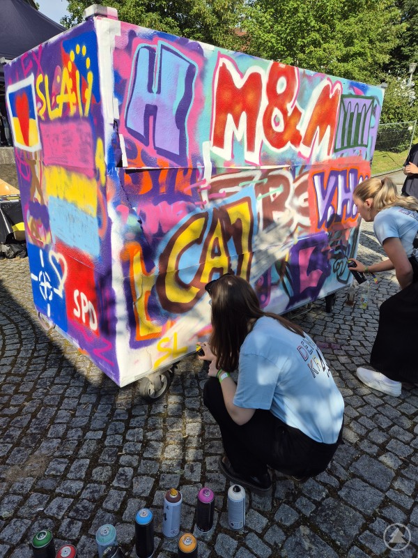 Jugendliche gestalten kreativ mit Spraydosen ein Graffiti auf einer Leinwand beim Fest-i-Wal 