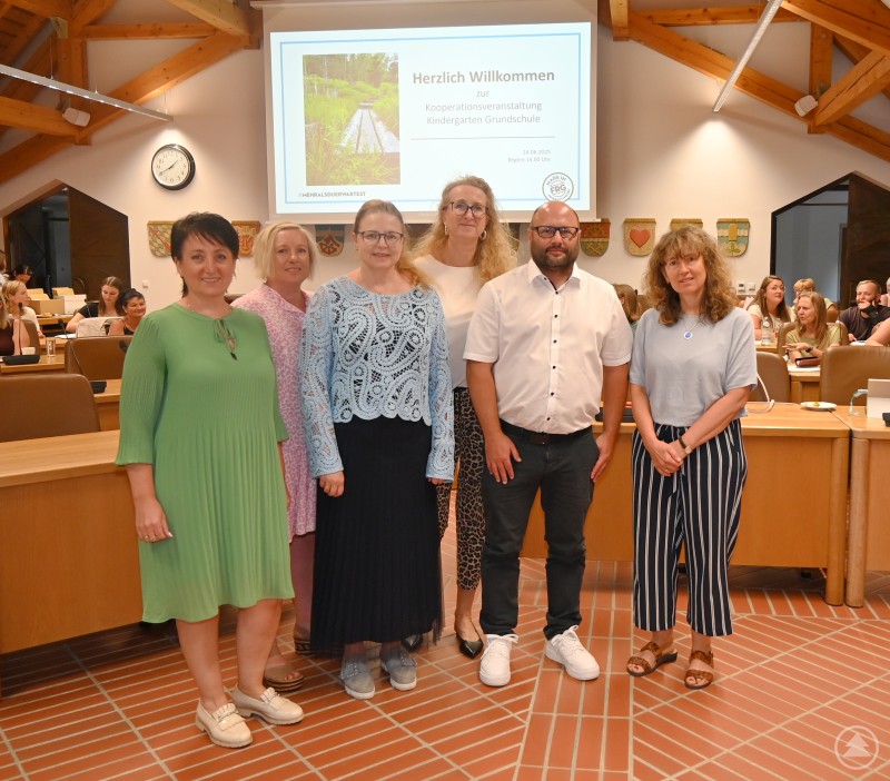 Informierten zum Thema Sprachförderung in Kindergarten und Schule (von links): Referentin Anna Petrilak-Weissfeld, Alexandra Stadler (Landratsamt), Beratungslehrerin Simone Springer, Kooperationsbeauftragte im Landkreis Rektorin Alexandra Bauer sowie die beiden Beratungslehrkräfte Alexander Donaubauer und Sabine Zitzl. Sechs Personen stehen im Sitzungssaal vor einer Präsentationsfolie zur Kooperation Kindergarten-Grundschule, im Hintergrund sitzen weitere Teilnehmende.