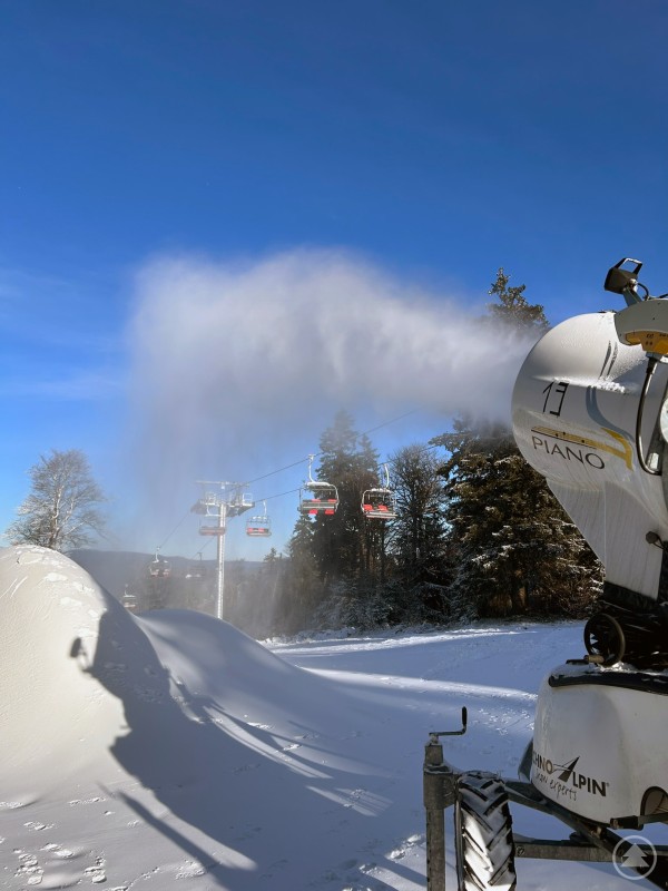 Moderne Beschneiung im Einsatz im Skizentrum Mitterdorf: Die modernisierte Beschneiungsanlage sorgt gemeinsam mit den neuen Liftanlagen für verlässliche Bedingungen im laufenden Winterbetrieb. Schneekanone im Einsatz vor einer Sesselbahn am verschneiten Hang bei strahlend blauem Himmel.
