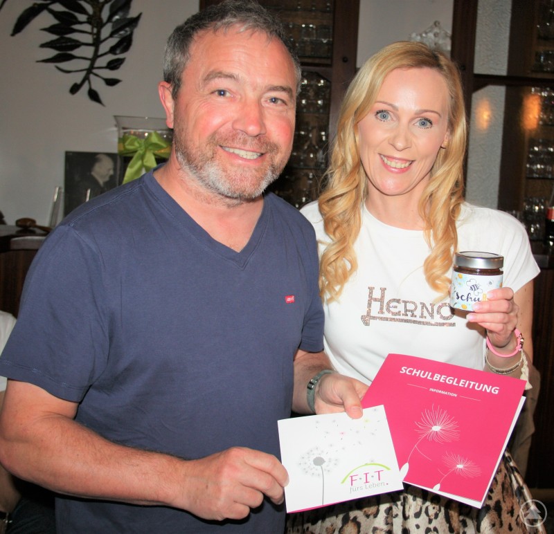 Das breite Tätigkeitsspektrum des in der Öffentlichkeit nahezu nicht bekannten Familien-Interventions-Team e.K. und die damit verbundenen großen aktuellen Herausforderungen stellte Inhaberin Katrin Weichselsdorfer (rechts) dem Rotary-Club Passau-Dreiflüssestadt vor. Dessen Präsident Peter Niedermeier (links) bedankte sich mit einem kleinen Präsent für die ausgiebige Möglichkeit zur Diskussion über die Aufgaben und Probleme der staatlichen Jugend- und Integrationsämter. Das Bild zeigt zwei fröhliche Personen, einen Mann und eine Frau, die gemeinsam Materialien und Produkte präsentieren. Die Frau hält ein Glas mit der Aufschrift „Schulbiene“ sowie eine pinke Infomappe mit dem Titel „Schulbegleitung“. Der Mann hält eine Karte mit dem Logo „FIT fürs Leben“. Beide scheinen in ein Projekt im Bereich Bildung, Schulbegleitung oder Lebenshilfe eingebunden zu sein – möglicherweise bei einer Informationsveranstaltung oder einem kleinen Event. Die Stimmung wirkt positiv und engagiert.