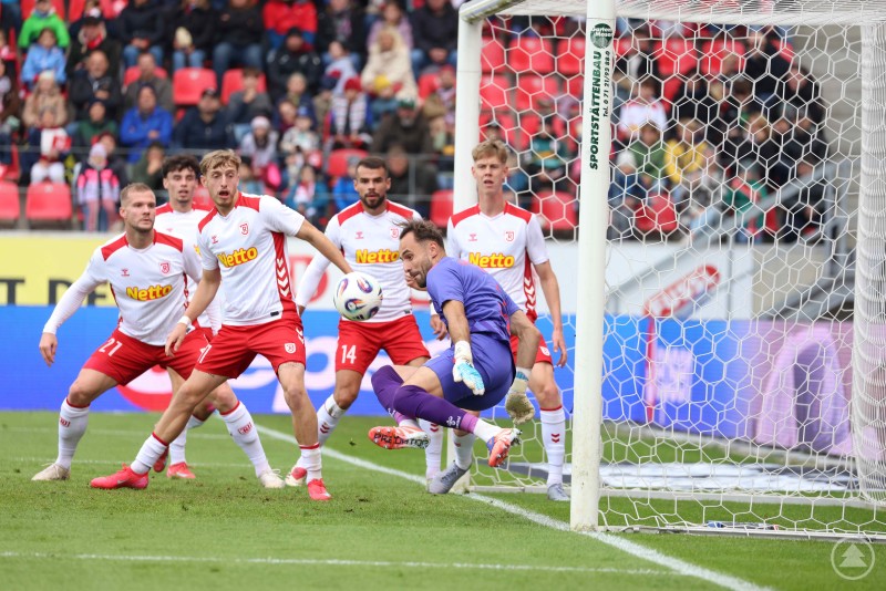 Jahn-Torhüter Jonas Gebhardt verhindert den Gegentreffer mit einer starken Parade. Mehrere Spieler des SSV Jahn Regensburg verteidigen vor dem eigenen Tor, während der Torhüter einen Ball abwehrt.