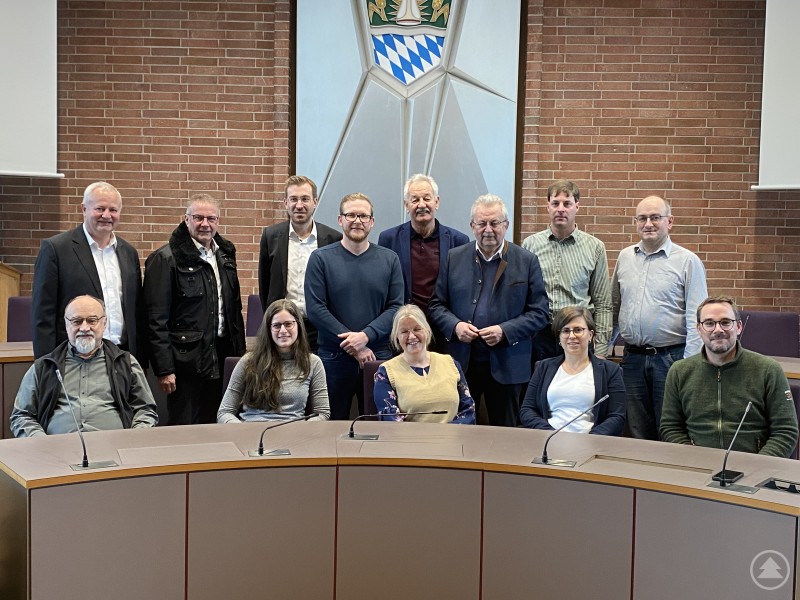 Die Mitglieder der Vorstandschaft und der Geschäftsführung beim Gruppenfoto am Rande der Mitgliederversammlung. Gruppenfoto im Sitzungssaal des Landratsamtes. Mehrere Personen stehen und sitzen vor einer gebogenen Tischreihe, im Hintergrund eine Backsteinwand mit Wappen.