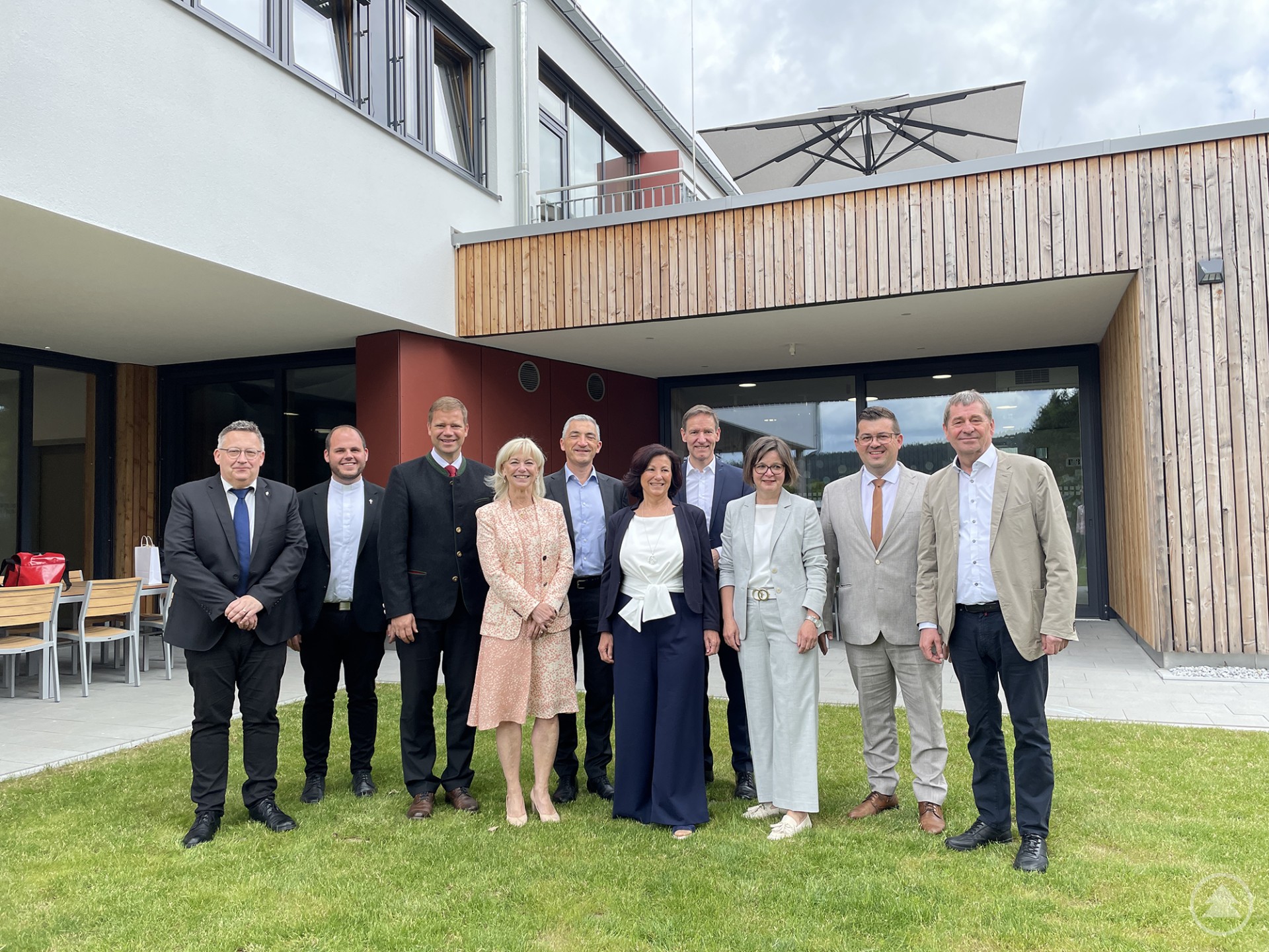 Freuten sich über die Einweihung: die beiden Pfarrer Matthias Schricker und Marco Stangl, Bezirkstagspräsident Dr. Olaf Heinrich, Lebenshilfe-Landesvorsitzende Carolina Trautner, Landrat Dr. Ronny Raith, Vorsitzende der Lebenshilfe Regen Bernadette Wagenbauer, Regierungspräsident Rainer Haselbeck, Geschäftsführerin der Lebenshilfe Regen Tanja Sixt, Bürgermeister Andreas Kroner und Geschäftsführer der Lebenshilfe Regen Jochen Fischer. Eine Gruppe von zehn Personen, darunter Vertreter der Lebenshilfe, Politiker und Geistliche, steht vor einem modernen Gebäude mit Holzfassade und großen Fenstern, lächelnd für ein Gruppenfoto.