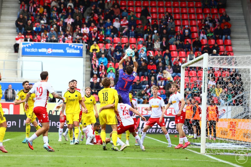 Der Torhüter des SSV Jahn Regensburg fängt eine Flanke im Strafraum, umgeben von Spielern beider Mannschaften.