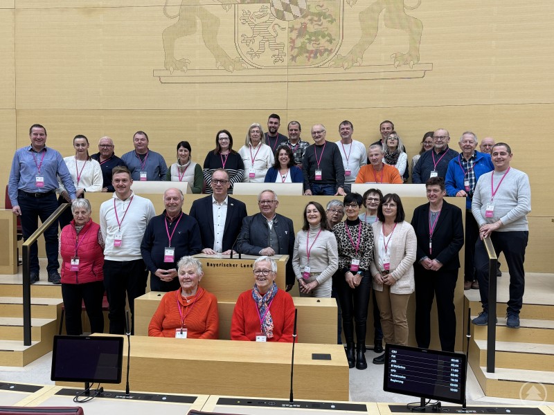 Besuchergruppe der Freien Wähler Spiegelau gemeinsam mit MdL Martin Behringer im Plenarsaal des Bayerischen Landtags. Eine große Besuchergruppe steht im Plenarsaal des Bayerischen Landtags auf den Sitzreihen verteilt. Vorne in der Mitte steht MdL Martin Behringer am Rednerpult. Alle tragen Besucherausweise; im Hintergrund ist das große bayerische Wappen an der Wand zu sehen.