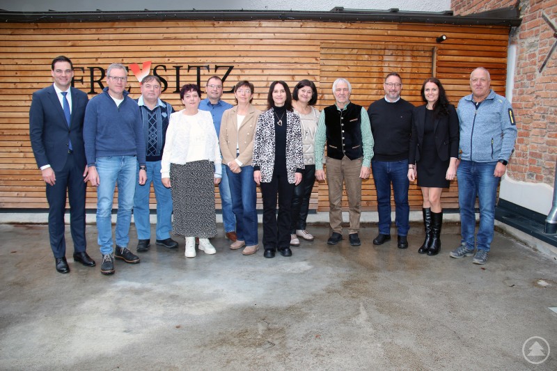 Landrat Sebastian Gruber mit den Geehrten v.l.: Thomas Eder, Josef Halser, Andrea Jakob, Herbert Poxleitner, Elfriede Wilhelm, Petra Allmannsberger, Claudia Freund, Max Seibold, Personalrat Alexander Bertelshofer, Carmen Traxinger und Walter Boxleitner. Eine Gruppe von zwölf Personen steht für ein gemeinsames Foto vor einer Holz- und Backsteinwand. Die Personen sind in einer Reihe angeordnet, tragen überwiegend Business- oder Freizeitkleidung und blicken freundlich in die Kamera.