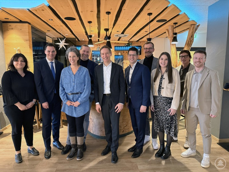 Eine Delegation aus zehn Personen, M&auml;nner und Frauen in Businesskleidung, steht gemeinsam in einem modern eingerichteten Raum. Alle blicken freundlich in die Kamera. Im Hintergrund sind Holzelemente und weihnachtliche Deko zu sehen.