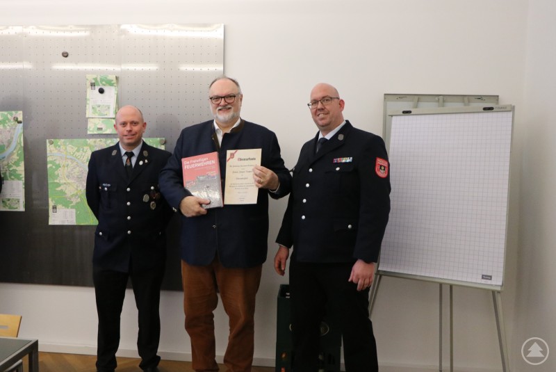 Oberbürgermeister Jürgen Dupper (3. von links) mit den Verantwortlichen der Feuerwehr Grubweg im Alten Rathaus. Eine Gruppe von Feuerwehrkameraden in Uniform sowie zwei zivile Gäste stehen gemeinsam in einem historischen Raum des Alten Rathauses. In der Mitte steht eine kleine Skulptur auf einem Sockel, während sich die Beteiligten zu einem Gruppenfoto aufgestellt haben.