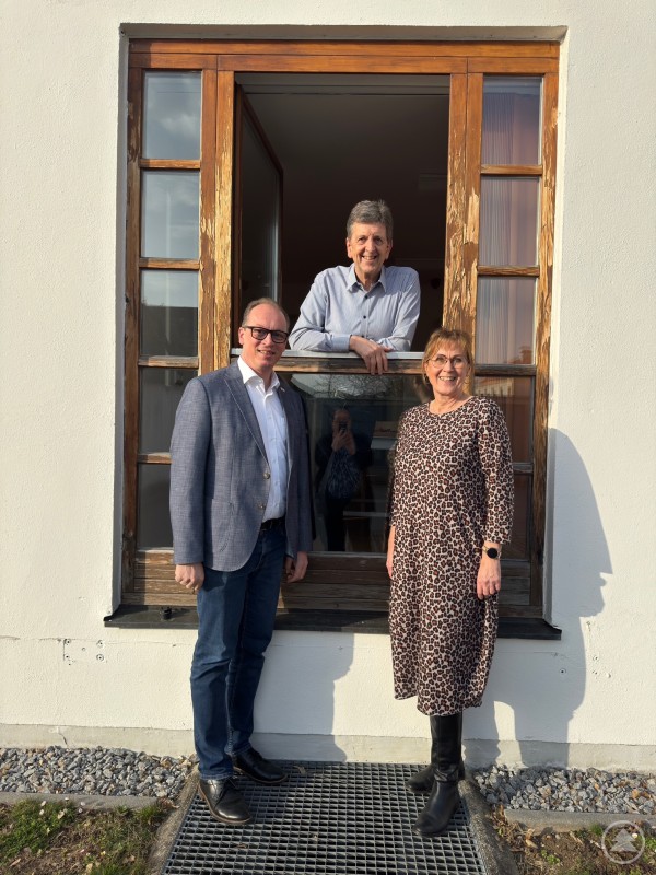 MdL Martin Behringer informierte sich gemeinsam mit Verantwortlichen vor Ort über den geplanten Austausch der alten Fenster an der Landvolkshochschule. Zwei Personen stehen vor einem geöffneten Fenster eines älteren Gebäudes, während eine dritte Person aus dem Fenster heraus nach außen schaut. Das Bild zeigt ein Holzfenster mit sichtbaren Gebrauchsspuren, das im Zuge einer geplanten Sanierung ersetzt werden soll.