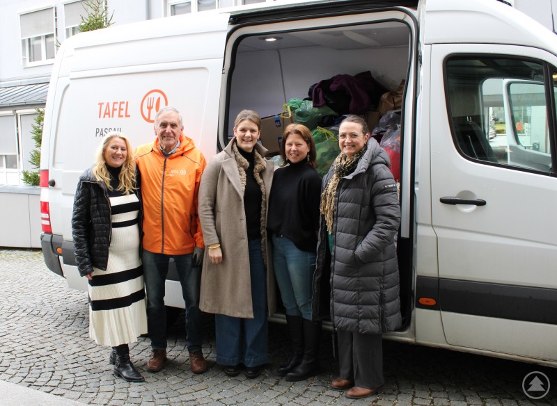 Mehrere Frauen und ein Mann stehen vor einem Transporter der Tafel, dessen Laderaum mit Spenden gef&uuml;llt ist. Die Gruppe posiert gemeinsam vor dem Fahrzeug.