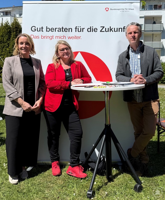 Beim Bewerbertag der Pro Seniore Residenz Wittelsbacherhöhe informierten Vertreter der Pflegeeinrichtung und der Agentur für Arbeit über Karrierechancen im Pflegebereich. Drei Personen stehen an einem Infostand der Bundesagentur für Arbeit im Freien. Sie informieren über Karriere- und Einstiegsmöglichkeiten im Pflegebereich.