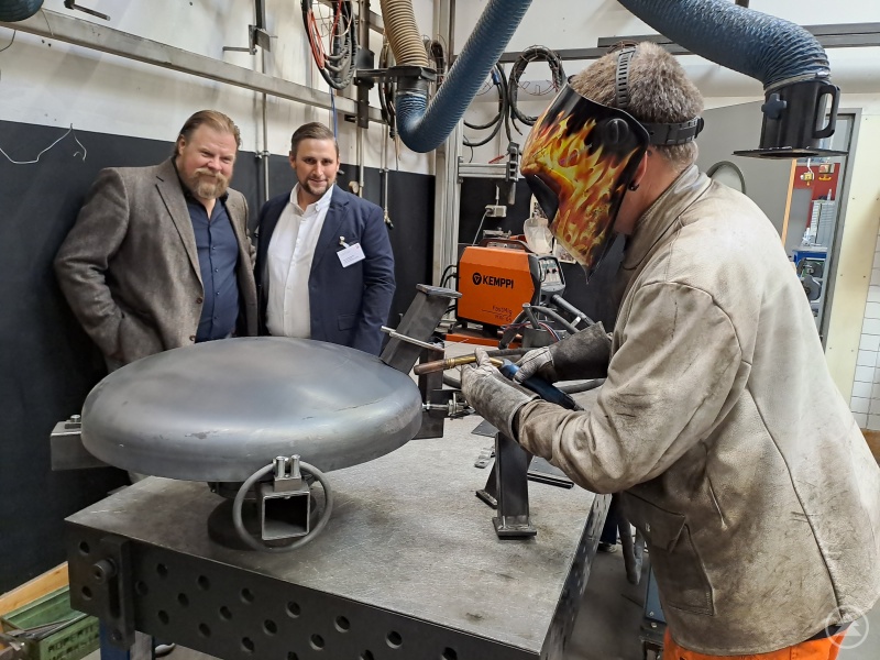Der Film- und Theaterschauspieler Michael Alexander Grimm, hier mit Werkstatt-Leiter Georg Bachmeier (re.) im Metallbereich, wie ein Mitarbeiter Feuerschalen schweißt.