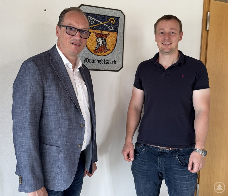 MdL Martin Behringer im Gespräch mit Bürgermeister Johannes Vogl in Drachselsried. Zwei Männer stehen nebeneinander in einem Büro vor einem Wappen der Gemeinde Drachselsried, beide lächeln in die Kamera.