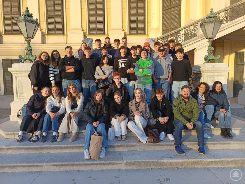 Bei strahlendem Sonnenschein genossen die Grafenauer Realschüler das Ambiente in Schloss Schönbrunn. Eine große Gruppe von Jugendlichen und Lehrkräften sitzt auf den Stufen vor Schloss Schönbrunn in Wien und posiert für ein gemeinsames Gruppenfoto bei sonnigem Wetter.