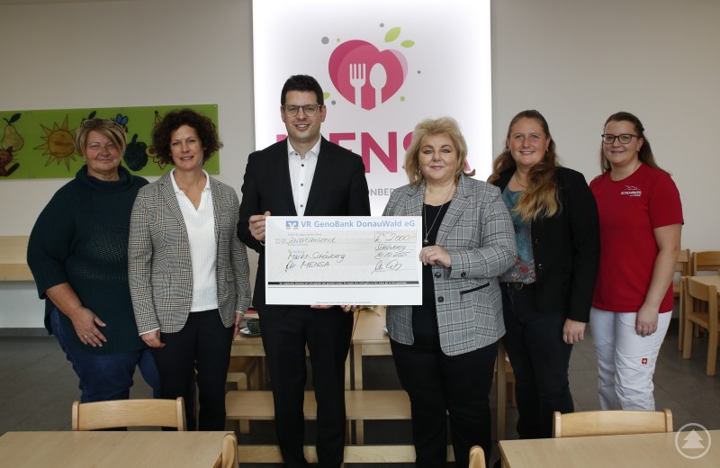 Einen Scheck über 2000 Euro übernahm Bürgermeister Martin Pichler von Geschäftsstellenleiterin Claudia Wildfeuer flankiert von Kindergartenleiterin Dani Luksch (v.l.), Bettina Marjanovic, die sich in der Marktverwaltung um Belange der Kleinsten kümmert, sowie Elisabeth Keskic-Biebl (v.r.) und Gemeinderätin Carina Bredl. Mehrere Frauen und ein Mann stehen in einem hellen Raum vor einem Logo der VR GenoBank. In der Mitte hält Bürgermeister Martin Pichler einen großen symbolischen Spendenscheck in den Händen. Alle Beteiligten lächeln in die Kamera.