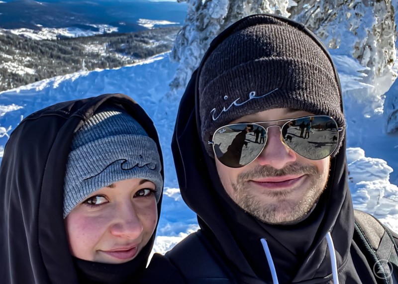 Jasmin und Niklas Feichtinger Jasmin und Niklas Feichtinger mit Nice Wave Mützen vor einer verschneiten Winterlandschaft und blauem Himmel.