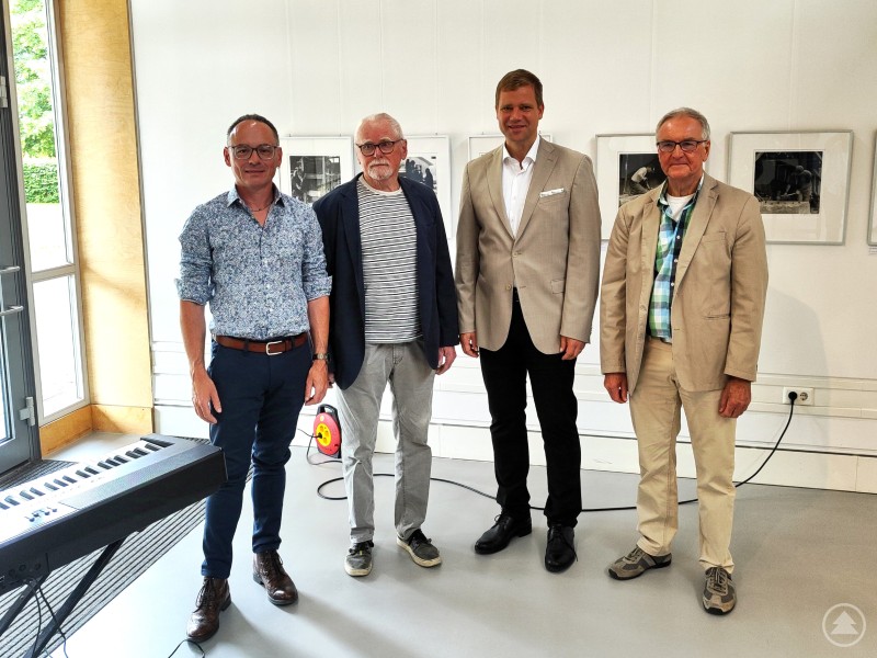 Bei der Eröffnung der Sonderausstellung „Analoges Handwerk“ im Freilichtmuseum Finsterau würdigte Bezirkstagspräsident Dr. Olaf Heinrich (2. v. re.) die Arbeiten von Fotograf Ernst Herrmann (2. v. li.), musikalisch begleitet von Sven Ochsenbauer (1. v. li.). Die Laudatio hielt Dr. Otto Stählin (1. v. re.). Vier Männer stehen in einer Ausstellung vor gerahmten Schwarz-Weiß-Fotografien; links im Bild steht ein E-Piano.