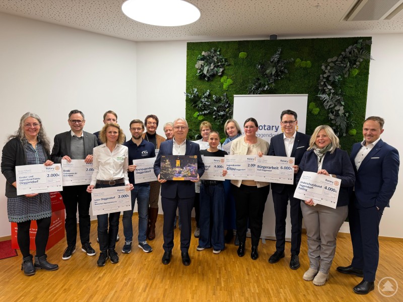 Das Rotary Hilfswerk Deggendorf e.V. überreichte im Rahmen einer Feierstunde die Spendenschecks an die Vertreterinnen und Vertreter der 13 begünstigten Organisationen. Vertreterinnen und Vertreter von 13 sozialen Einrichtungen stehen gemeinsam mit Mitgliedern des Rotary Hilfswerks Deggendorf in einem modern gestalteten Raum. Sie halten große symbolische Spendenschecks in den Händen und posieren für ein Gruppenfoto nach der offiziellen Spendenübergabe.