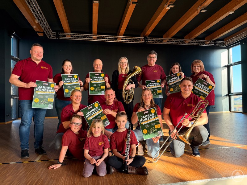 Die Mitwirkenden aus Musik, Tanz und Gesang freuen sich auf das Jahreskonzert am 28. März 2026 – neuer Termin: Samstag vor dem Palmsonntag. Gruppenfoto der Mitwirkenden aus Musik, Tanz und Gesang mit Instrumenten und Konzertplakaten in einem Saal