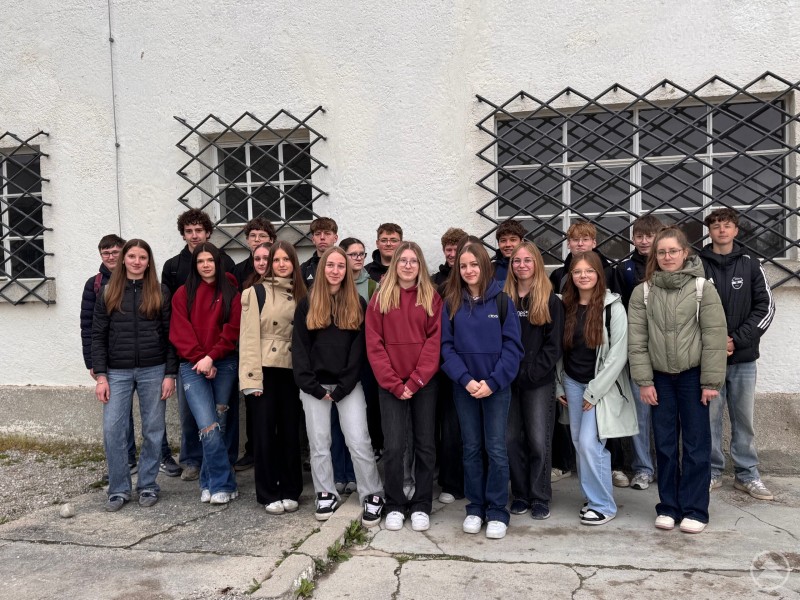 Die Schülerinnen und Schüler der neunten Klassen des LLG beim Besuch der Gedenkstätte Dachau Schulklasse steht vor einer Hauswand mit vergitterten Fenstern und blickt in die Kamera