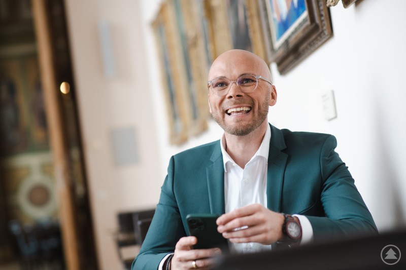 Staatsminister Dr. Fabian Mehring ist am 16. Mai 2025 zu Gast im GreG in Freyung ChatGPT: Das Bild zeigt einen gut gelaunten Mann im Anzug, der in einem elegant eingerichteten Raum mit historischen Gemälden an der Wand sitzt. Er hält ein Smartphone in der Hand und lächelt offen – die Szene wirkt authentisch und sympathisch. Der Mann auf dem Bild ist Dr. Fabian Mehring, Bayerischer Digitalminister. Die Aufnahme entstand vermutlich im Rahmen einer Veranstaltung zur Digitalisierung im ländlichen Raum, bei der er als Redner oder Gesprächspartner aktiv war. Das Umfeld deutet auf eine kulturell bedeutsame oder offizielle Location hin.
