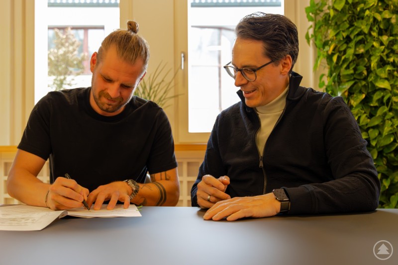 Oberbürgermeister Dr. Christian Moser und Pächter Florian Heidel unterzeichnen den Pachtvertrag für den neuen Donaugarten Zwei Männer sitzen an einem Tisch und unterschreiben gemeinsam Dokumente. Beide wirken konzentriert und zufrieden, während im Hintergrund Fenster und Pflanzen zu sehen sind.