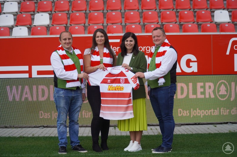 Andreas Bildl, Amelie Fuchs, Simone Piller und Stefan Behringer im Jahnstadion Regensburg. BWmedien ist offizieller Klassik Partner des SSV Jahn Regensburg. Vier Personen – Andreas Bildl, Amelie Fuchs, Simone Piller und Stefan Behringer – stehen im Jahnstadion Regensburg und präsentieren gemeinsam die Partnerschaft zwischen BWmedien und dem SSV Jahn Regensburg.