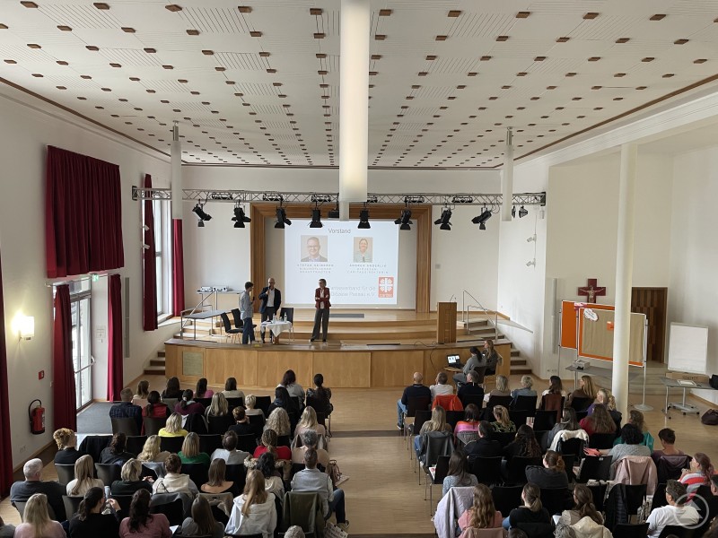 Caritas-Vorstand Stefan Seiderer und Caritasdirektorin Andrea Anderlik begrüßten gemeinsam die neuen Mitarbeitenden und stellten die Werte und Aufgaben der Caritas vor. Ein Vortragssaal mit vielen Zuhörer:innen, die aufmerksam einer Präsentation folgen. Auf der Bühne sprechen drei Personen, hinter ihnen ist eine Leinwand mit dem Logo des Caritasverbandes Passau zu sehen.