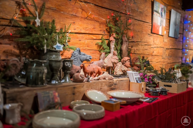 Kunsthandwerk mit Herz: Beim Adventsmarkt im Alten Rathaus Bodenmais präsentieren regionale Künstlerinnen und Künstler ihre Arbeiten. Ein liebevoll dekorierter Tisch mit handgefertigter Keramik, Tonfiguren und weihnachtlichen Gestecken steht vor einer rustikalen Holzwand. Warmes Licht und kleine Lichterketten sorgen für festliche Stimmung.