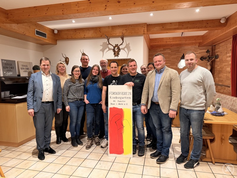 v.L. Bürgermeister Alexander Mayer, Kindergartenleiterin Barbara Klessinger, Maria Brunner, Stefan Brunnbauer, Martina Stix, Stadtrat Erwin Liebl, 2. Vorsitzender Matthias Schwarz, Carolin Lehner, der neue 1. Vorsitzende Tobias Bauer, Alexandra Streifinger, Kerstin Haas, Stadtrat Stefan Behringer, der bisherige 1. Vorsitzende Stefan Haas Gruppenfoto der neu gewählten Vorstandschaft des Fördervereins Kindergarten Hl. Familie Haus i. Wald e.V. in einem Gastraum, mehrere Personen stehen nebeneinander und halten ein Vereinsbanner.