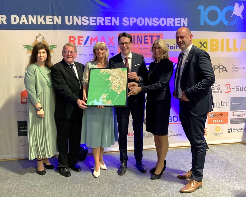 Symbol der Verbundenheit: Deggendorfs OB Dr. Christian Moser übergibt an die Partnerstadt ein 3D-Stadtmodell von Neusiedl anlässlich 100 Jahre Stadterhebung Neusiedl am See, von links: 1. Vizebürgermeisterin Sabine Nyikos Neusiedl, 2. Bürgermeister Günther Pammer Deggendorf, Bürgermeisterin und LAbg. Elisabeth Böhm, Oberbürgermeister Dr. Christian Moser, 3. Bürgermeisterin Renate Wasmeier Deggendorf und 2. Vizebürgermeister Stefan Wögerer Neusiedl Sechs Personen stehen bei einer Veranstaltung auf einer Bühne vor einer Sponsorenwand. In der Mitte wird ein gerahmtes 3D-Stadtmodell übergeben, während alle Beteiligten in die Kamera lächeln.