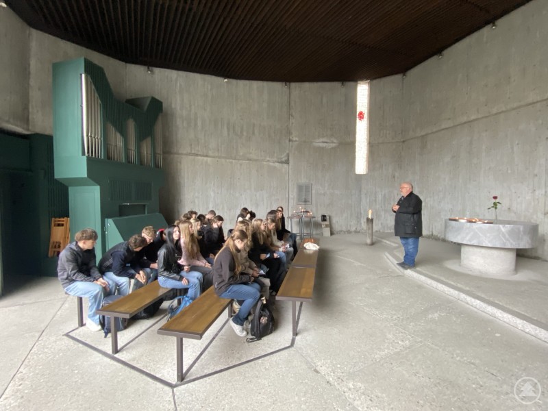 Besonders die Botschaft von Max Mannheimer "Nie wieder" bleibt hängen Gruppe von Schülerinnen und Schülern sitzt in einer Kapelle, ein Mann spricht vorne, ruhige und nachdenkliche Atmosphäre