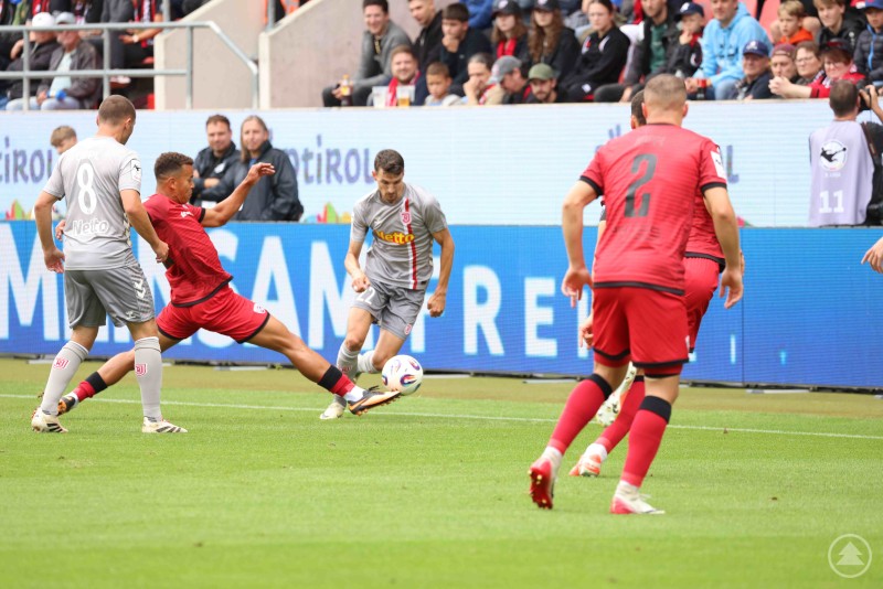 Fußballspieler des FC Ingolstadt und des SSV Jahn Regensburg im Zweikampf nahe der Seitenlinie, zahlreiche Zuschauer im Hintergrund.