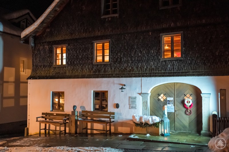 Das festlich beleuchtete Alte Rathaus in Bodenmais lädt zum Adventsmarkt ein. Das Kulturzentrum Altes Rathaus in Bodenmais zeigt sich am Abend winterlich beleuchtet. Vor dem Eingang liegen Schnee und eine Laterne, im Inneren strahlen warme Lichter.