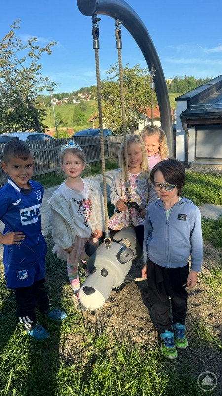 Mehrere Kindergartenkinder stehen lachend um ein neues Spielger&auml;t in Form eines Schaukelwolfs auf dem Au&szlig;engel&auml;nde des Kindergartens.