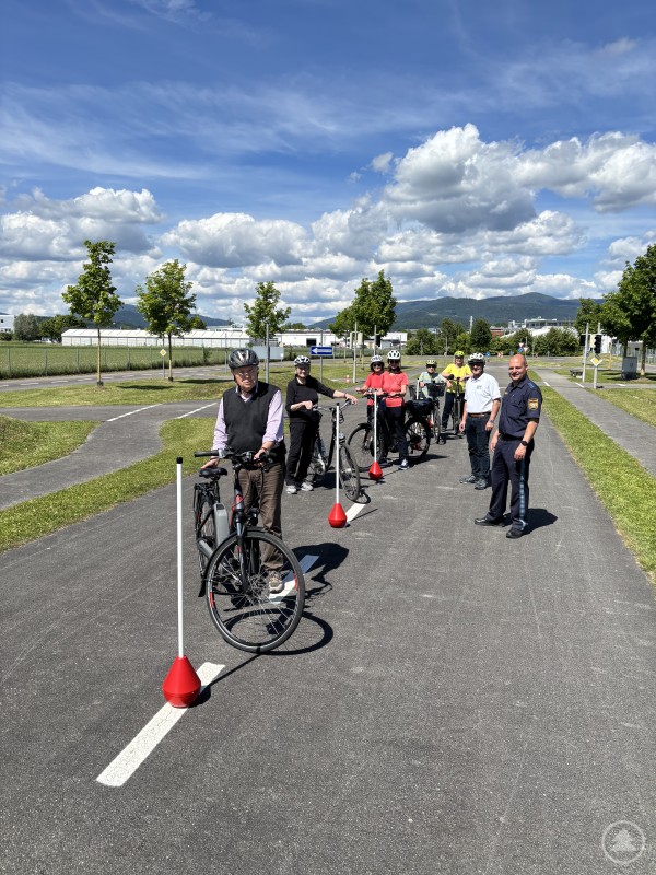 PHM Andreas Pilsl mit den Teilnehmern des Pedelec-Kurses Eine Gruppe von Senioren mit Helmen steht mit Pedelecs in einer Reihe auf einem Verkehrsübungsplatz, begleitet von einem Polizeibeamten.