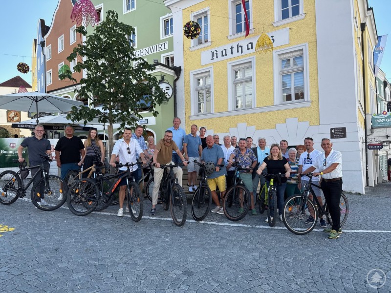Die Gemeinderatsmitglieder radelten oder gingen zu Fuß zur GEHmeindeRADsitzung und versammelten sich vor dem Rathaus in Schärding. Zahlreiche Gemeinderatsmitglieder mit Fahrrädern vor dem gelben Rathausgebäude der Stadt Schärding, teils in Alltagskleidung.