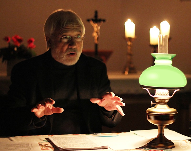 Ein älterer Mann mit grauem Haar und Bart liest bei Kerzenschein an einem Tisch. Eine grüne Öllampe und Kerzen tauchen die Szene in warmes Licht.