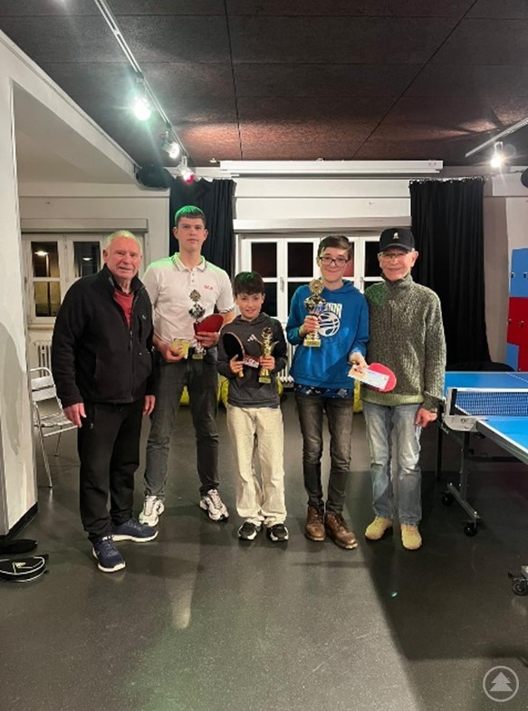 Franz Mayer, 3. Platz Mikita Panishev, 1. Platz Jakob Schmid, 2. Platz Matthias Resch, Alex Dik Gruppenfoto im Jugendcenter 4You: Fünf Personen stehen in einem Raum neben einer Tischtennisplatte, drei davon halten Pokale.