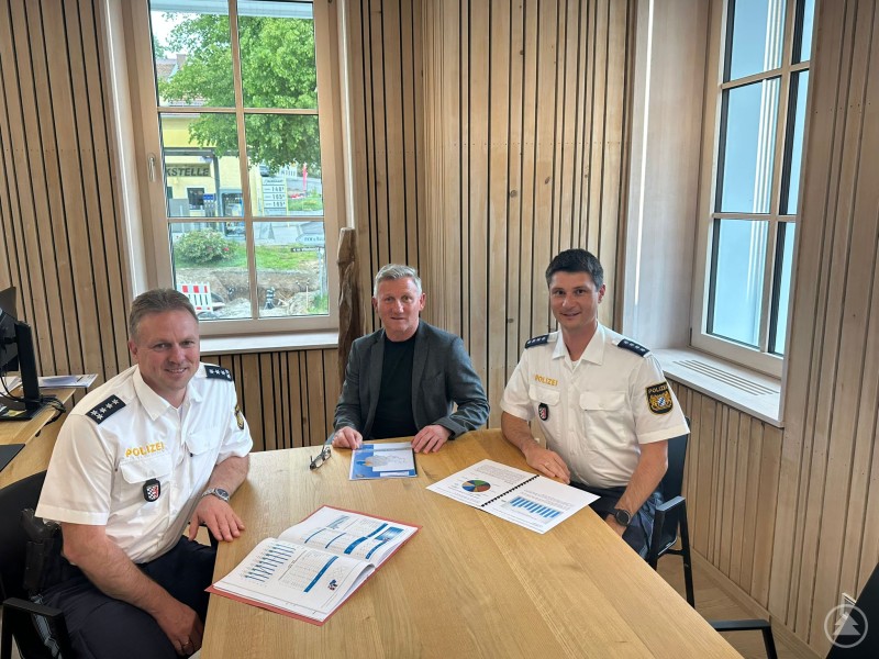 EPHK Thomas Kern, Bürgermeister Alfons Schinabeck und PHK Franz Weinzierl bei der Präsentation des Sicherheitsberichts. Drei Männer – zwei Polizisten in Uniform und ein Bürgermeister in Zivil – sitzen mit Berichten an einem Tisch in einem modernen Raum mit Holzverkleidung.