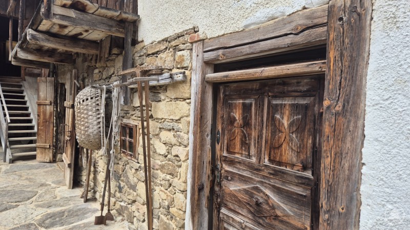 Eingang in das Wohnstadlhaus Eingang in den Hof mit alter verzierter Holztür, Steinmauer und alten Gerätschaften wie Rechen.