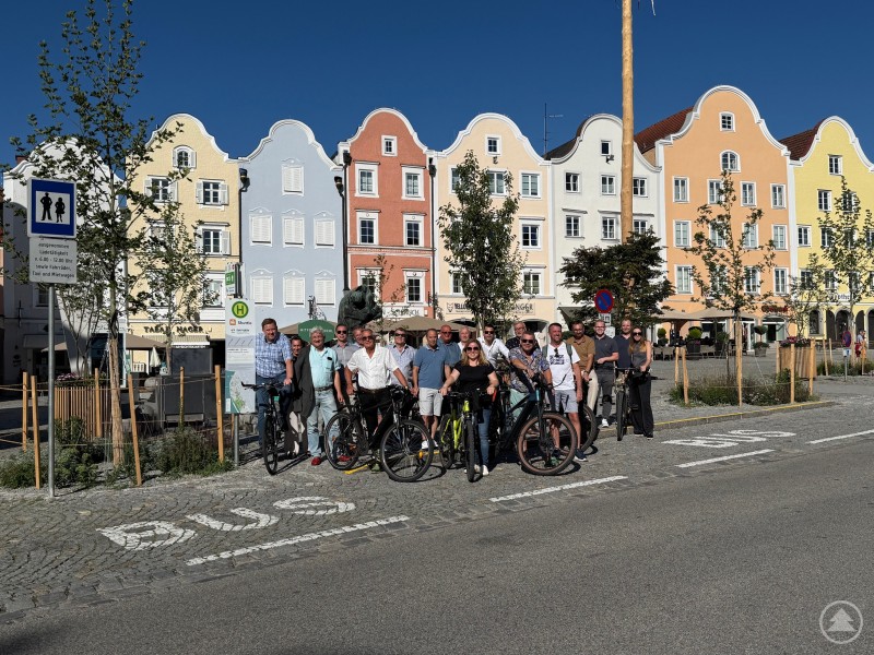 Die Gruppe steht mit Fahrrädern vor bunten barocken Häuserfassaden am zentralen Stadtplatz bei sonnigem Wetter.