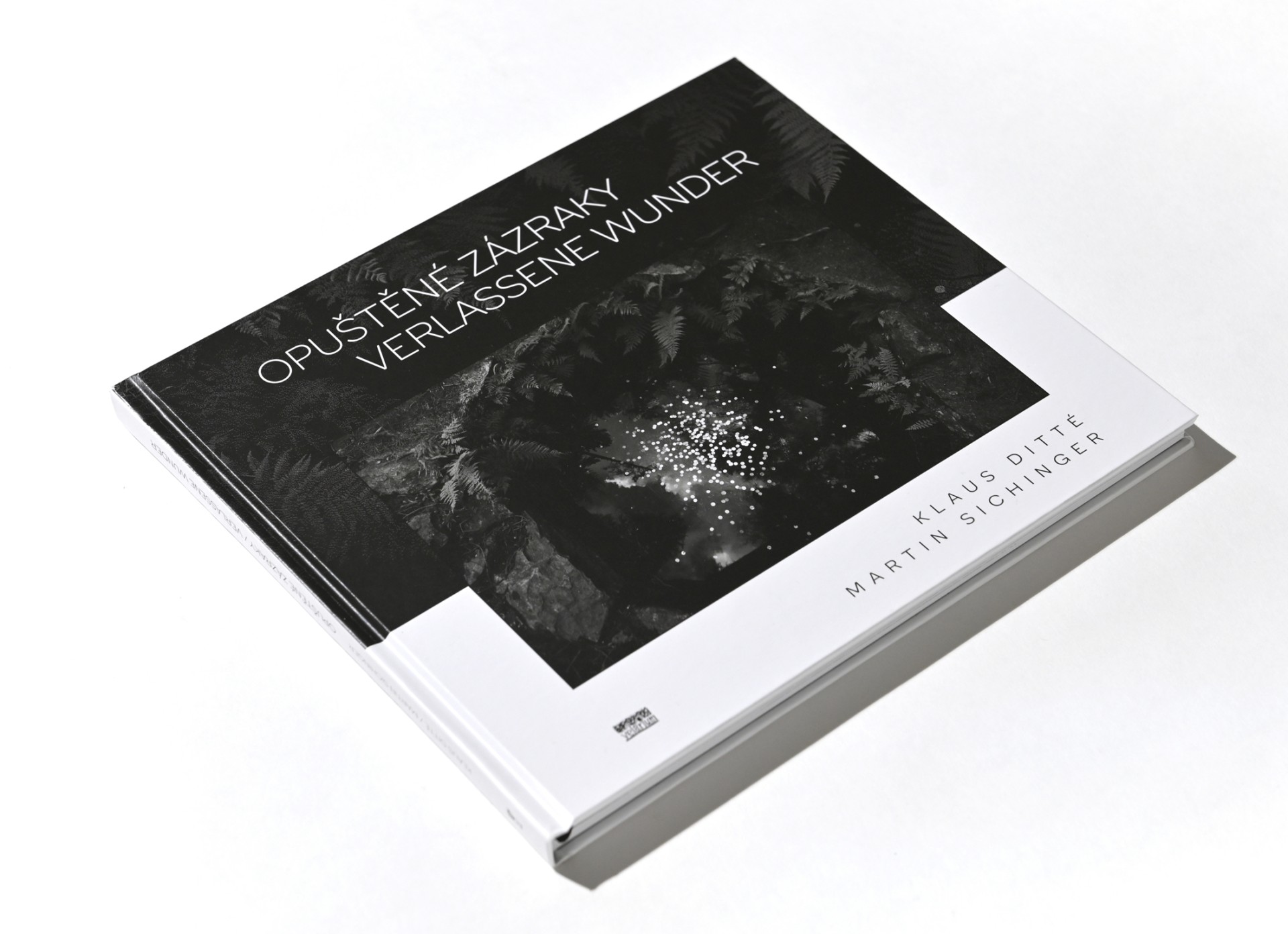 Ein aufgeschlagenes Buch mit dem Titel „Opuštěné zázraky / Verlassene Wunder“, gestaltet in Schwarz-Weiß mit einem zentralen Foto auf dem Cover.