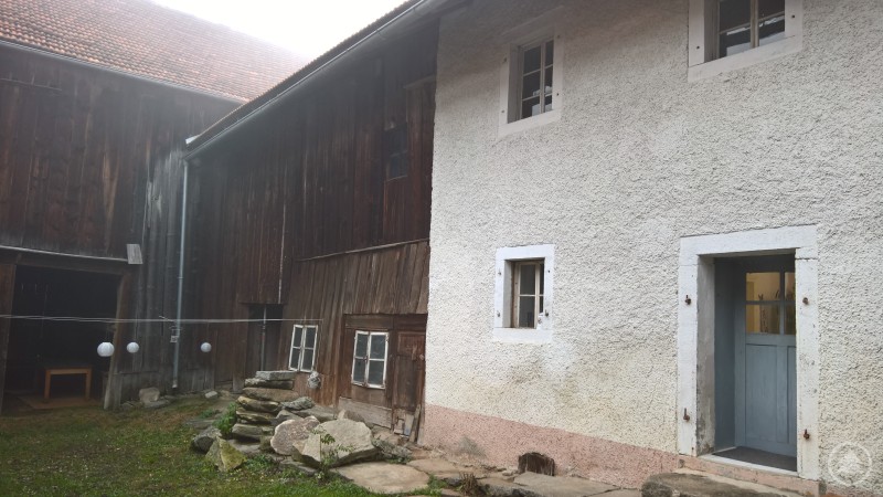 Blick auf das Bauernhaus und die angrenzende Scheune vor der Sanierung mit verwittertem Holz und Putz.