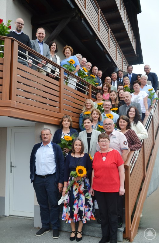 Die Kliniken Am Goldenen Steig ehrten ihre Dienstjubilare im Rahmen einer feierlichen Veranstaltung im Gasthaus Riedl in Kapfham. Gruppenbild auf einer Treppe mit zahlreichen Mitarbeitenden der Kliniken Am Goldenen Steig, die für ihre langjährige Betriebszugehörigkeit geehrt wurden. Viele halten Sonnenblumen in der Hand.